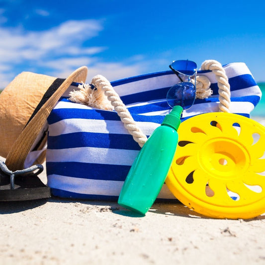 Beach essentials like straw hat, sunglasses, sunscreen and a beach bag, sitting on the sand