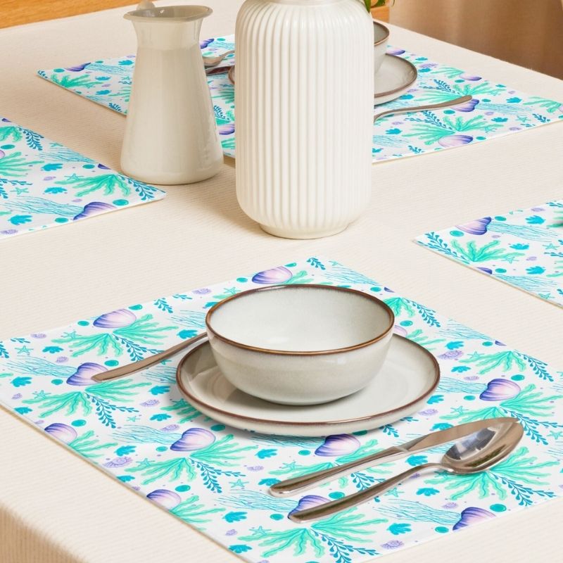 Dining table setting with coastal placemats, bowls, and cutlery on a wooden table. The placemats are colorful with aqua and lavender ocean inspired jellyfish