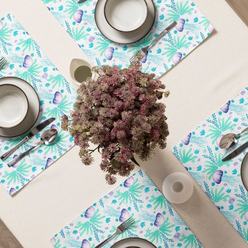 Table setting with floral centerpiece and ocean inspired coastal placemats with jellyfish and sea grasses