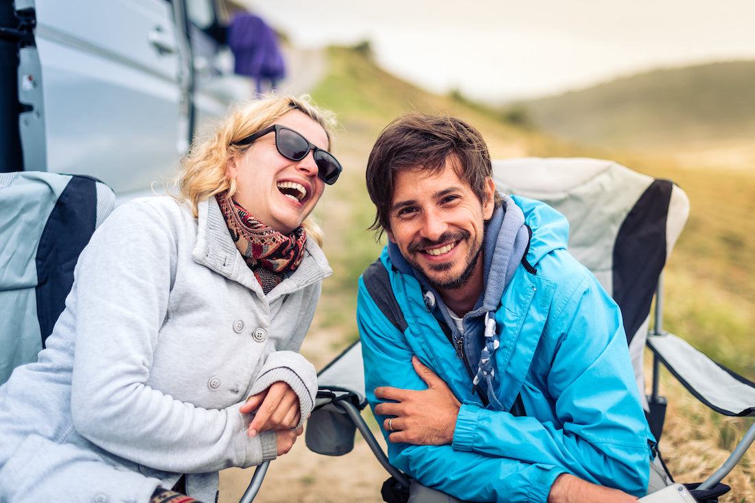 a lady and a man laughing in camp chairs outside at a campsite