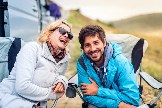 a lady and a man laughing in camp chairs outside at a campsite