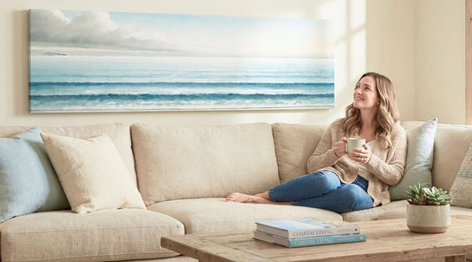 Coastal canvas wall art with endless ocean horizon, featured above a living room sofa with a woman relaxing and enjoying the view. Ideal for relaxation and home decor.