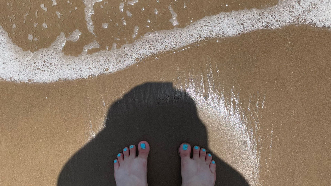 white bubbles of surf and two feet surrounded by a shadow of the person taking the picture form above