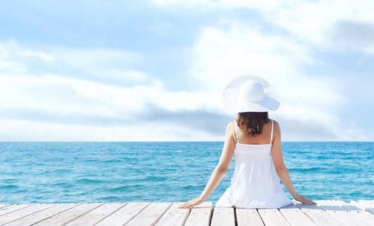 A woman sitting on a deck overlooking the blue ocean.