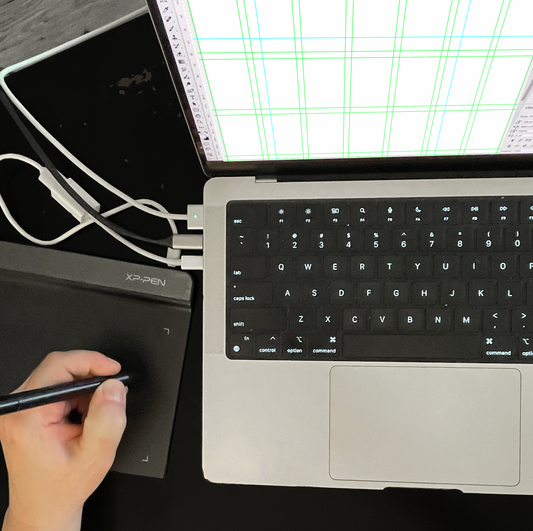 top down view of a laptop with gridlines on the screen and a hand holding smart pen on a pen tablet