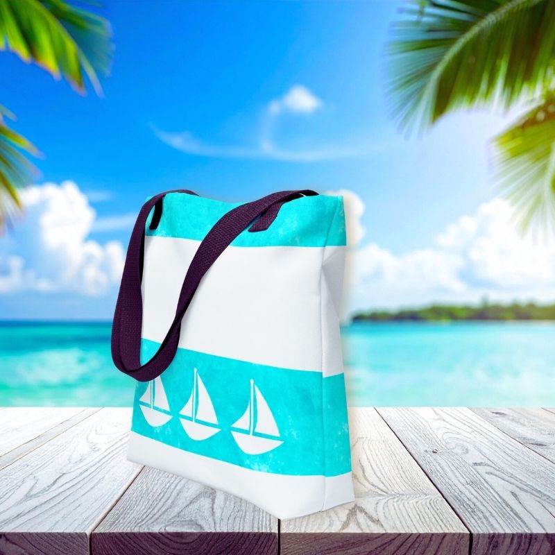 Side view of beach tote handbag with turquoise watercolor accents and sailboat motifs, styled against a tropical ocean backdrop.
