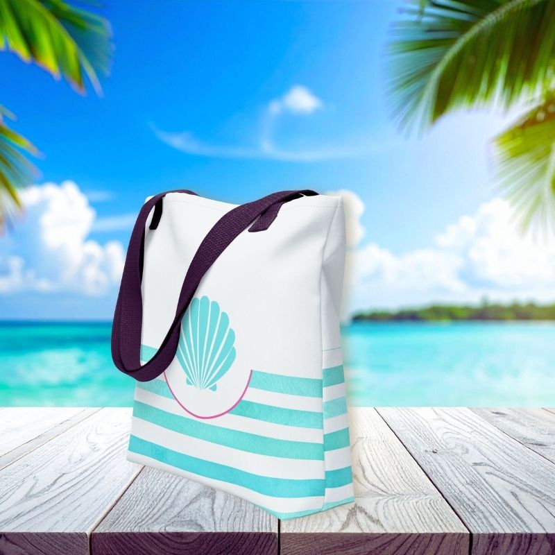 Side view of teal tote bag with turquoise seashell detail and stripe accents, styled against a tropical ocean backdrop.
