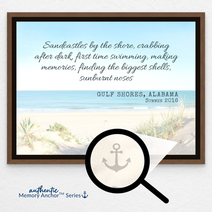A framed canvas print with memory from Gulf Shores, Alabama. A magnifying glass graphic zooms in on the bottom right corner of the art to reveal a subtle, hidden anchor icon within the sand design. The graphic is labeled "Authentic Memory Anchor™ Series" with the tagline "So your best beach memories never fade."
