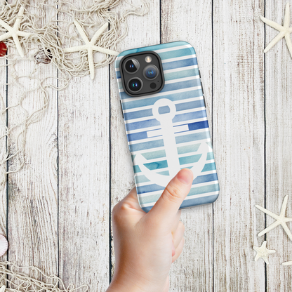 Hand holding a coastal phone case iPhone design with navy and aqua stripes and a large white anchor, styled on a wood background with nautical netting and starfish.